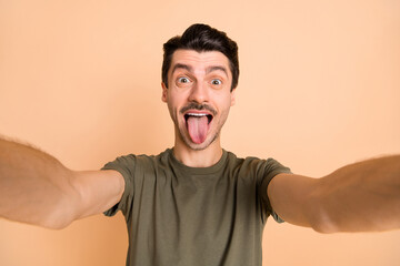 Photo of young funky funny smiling positive childish man showing tongue taking selfie isolated on pastel color background