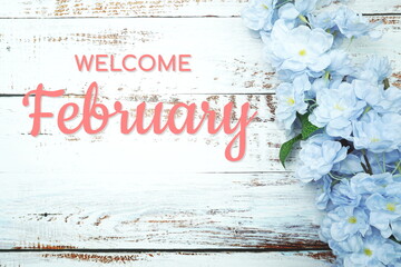 Welcome February text and blue flower decoration on wooden background