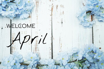 Welcome April text and blue flower decoration on wooden background
