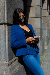 Young woman chatting with her smartphone. She wears mask,  jeans and an blue American jacket. The photo was taken in La Laguna, Tenerife. 