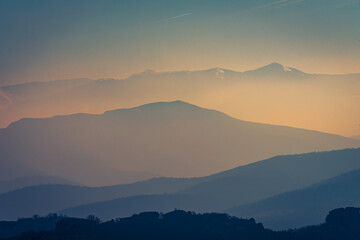 Fototapeta na wymiar Hazy sunrise over the silhouettes of the mountains 