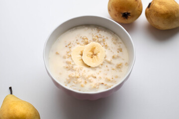 Bowl of oatmeal porridge with banana slices on white table. Healthy breakfast, diet food
