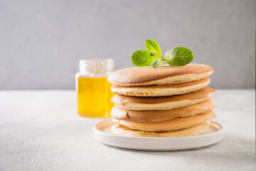 Sweet homemade stack of pancakes with honey and mint on a white background. Space for text.
