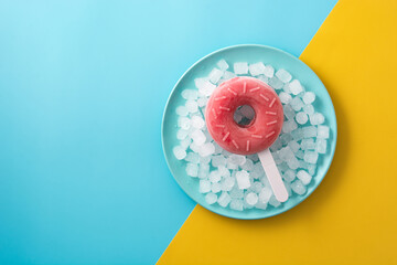 Obraz premium Strawberry donut popsicle and crushed ice on yellow and blue background. Copy space