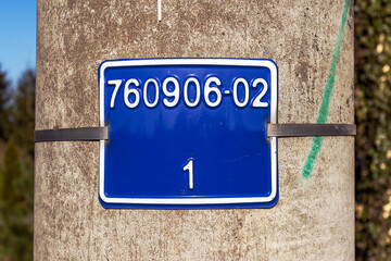 Metalowa tablica z numerami na słupie betonowym.