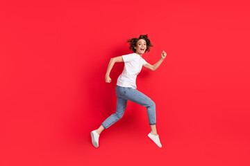 Full length body size profile side view of attractive cheerful girl jumping running isolated over bright red color background