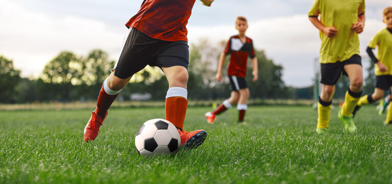Soccer player kicking ball in game. Group of School kids playing football on grass field