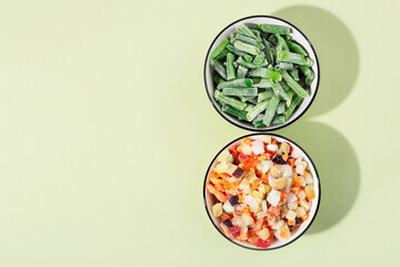 frozen vegetable mixture in a bowl on a green background, top view, hard light, shadows