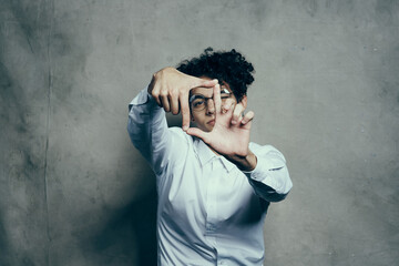 fashionable guy with curly hair gesturing with his hands on a gray background portrait close-up