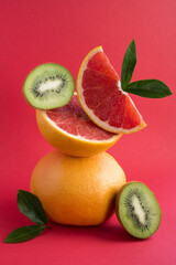 Pyramid of grapefruit and  kiwi in balance  on the red background.Close-up. Location vertical.