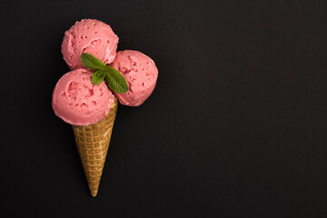 Top view of strawberry ice cream in a waffle cone on the black background. Close-up. Copy space.