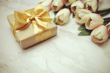 Obraz na płótnie Canvas Gift boxes with gold ribbon and tulip flower bouquet on marble background