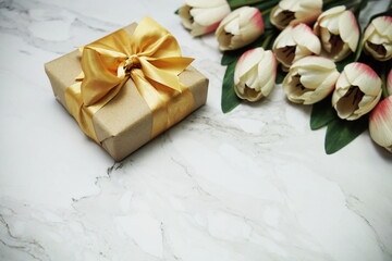 Fototapeta na wymiar Gift boxes with gold ribbon and tulip flower bouquet on marble background