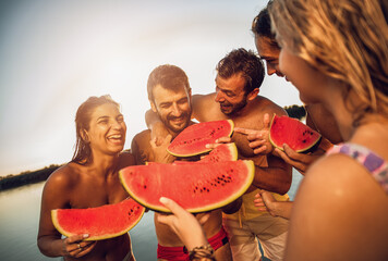 Friends standing on a pier eating watermelon and enjoying a summer day at the lake.