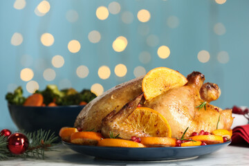Delicious chicken with oranges and pomegranate on white table against blurred festive lights
