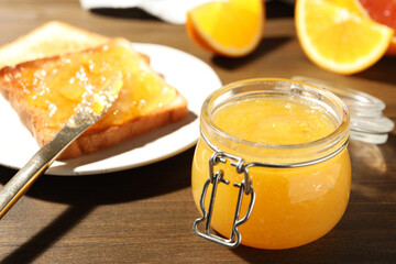 Delicious orange marmalade and toasts on wooden table