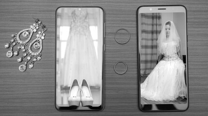 wedding accessories, a phone with a photo of a wedding dress next to earrings and wedding rings, marriage registry. Black and white photo.  Phone of the bride and groom.