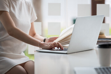 Cropped photo hand of woman writing making list taking notes in notepad working or learning online with laptop at home