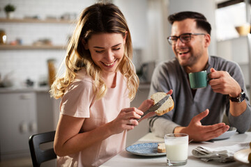 Beautiful woman enjoying in breakfast with her boyfriend. Happy young couple drinking coffee and eating sandwich at home..
