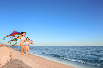 Obraz na płótnie Canvas Cute little girls flying rainbow kite on sea beach