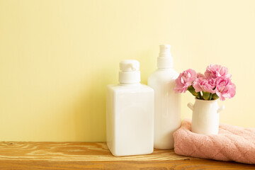 Fototapeta na wymiar Skin care and spa concept. Bathroom bottles and towel with pink flowers on wooden shelf. yellow background