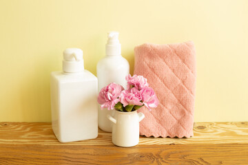 Obraz na płótnie Canvas Skin care and spa concept. Bathroom bottles and towel with pink flowers on wooden shelf. yellow background