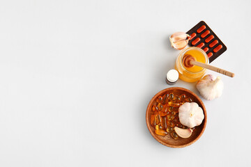 Fresh garlic with honey and pills on light background