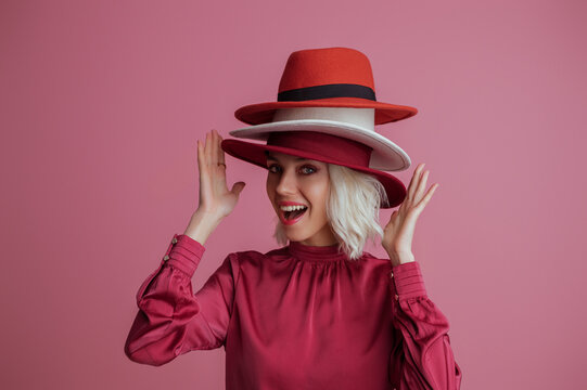 Funny, happy smiling fashionable  woman wearing many hats, posing on pink background. Model looking at camera. Fashion, sale, shopping advertising conception. Copy, empty space for text