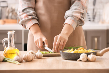 Obraz na płótnie Canvas Woman cutting green onion on table in kitchen