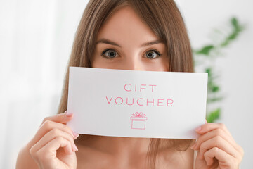 Beautiful young woman with gift voucher at home