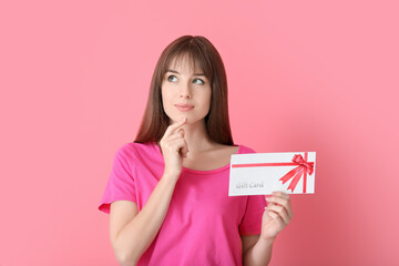 Thoughtful young woman with gift card on color background