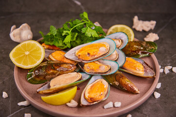 Fresh mussels in the sink lie on a large plate with parsley and lemon, on a dark gray table, sea salt is poured around the shells. The concept of healthy food and fresh seafood and delicacies.