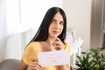 Thoughtful young woman with gift voucher at home