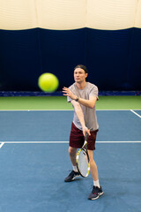 Male player in action on the indoor court playing tennis and beating the ball with a racket
