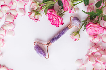 The front roller is made of amethyst on a white background with pink roses. Massager for lifting the skin made of natural stone. Beauty tools.