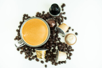 Espresso coffee in a cup surrounding with medium dark roasted coffee beans and coffee capsule