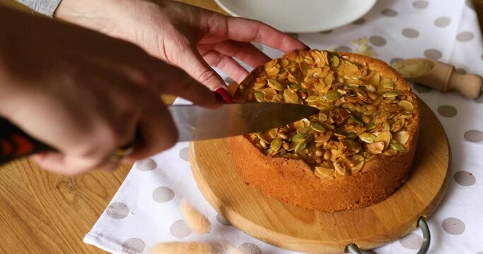 Hands of unrecognizable woman cutting apple or pear pie with caramel nuts on wooden table.