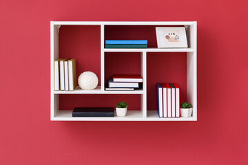 Shelf with books and decor hanging on color wall