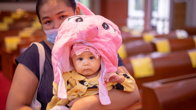 Young Asian Baby Girl Trying On Large Stuffed Animal Hat That's Too Big For Her Head