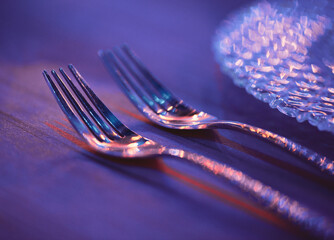 Two forks on a wooden table by a plate of glass