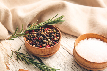 Bowls with mixed peppercorns, salt and rosemary on light wooden background