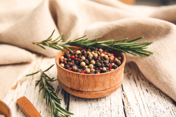 Bowl with mixed peppercorns and rosemary on light wooden background