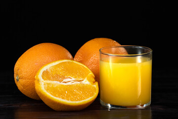 glass of fresh orange juice and oranges on a vintage dark wooden background