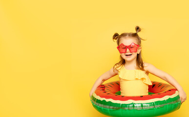 Little child girl in swimsuit and red funny sunglass with inflatable swimming colored ring posing on yellow studio background. Summer travel vacation with children concept.Banner,mock up,copy space