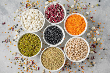 Mix of legumes, chickpeas, lentils, beans in bowls on a gray concrete background. Healthy, vegan and gluten free food. Top view. Copy space.