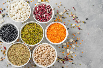 Mix of legumes, chickpeas, lentils, beans in bowls on a gray concrete background. Healthy, vegan and gluten free food. Top view. Copy space.