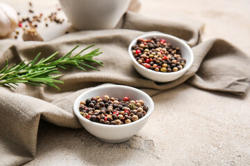 Bowls with mixed peppercorns and rosemary on light background
