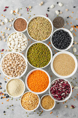 Mix of legumes, chickpeas, lentils, beans, peas, quinoa, sesame, chia, flax seeds in bowls on a gray concrete background. Top view.