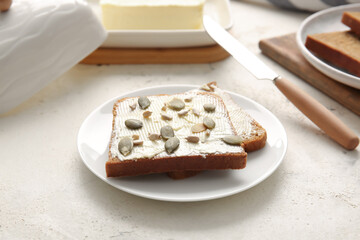 Slices of fresh bread, butter and seeds on light background