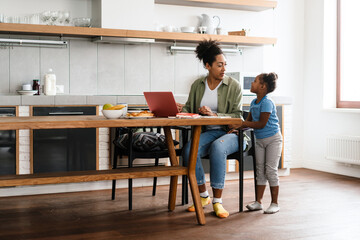 Black woman talking with her daughter while working with laptop